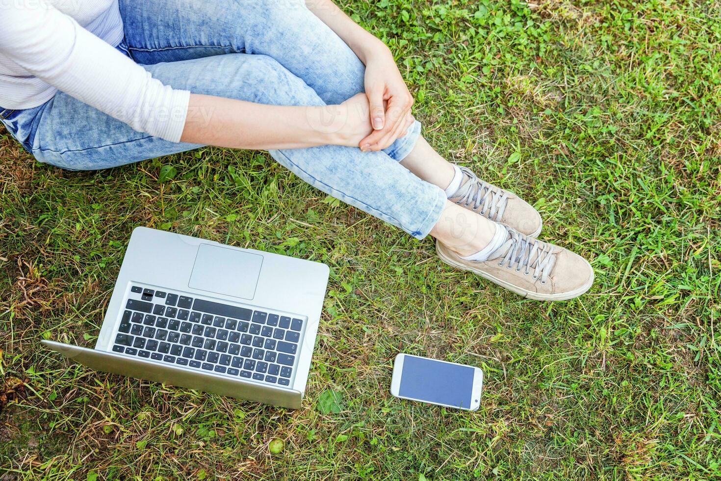 Woman legs on green grass lawn in city park, hands working on laptop pc computer. Freelance business concept photo
