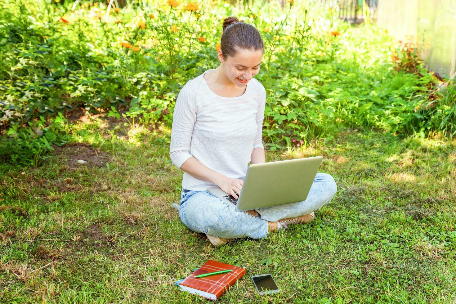 Young woman sitting on green grass lawn in city park working on laptop pc computer. Freelance business concept photo
