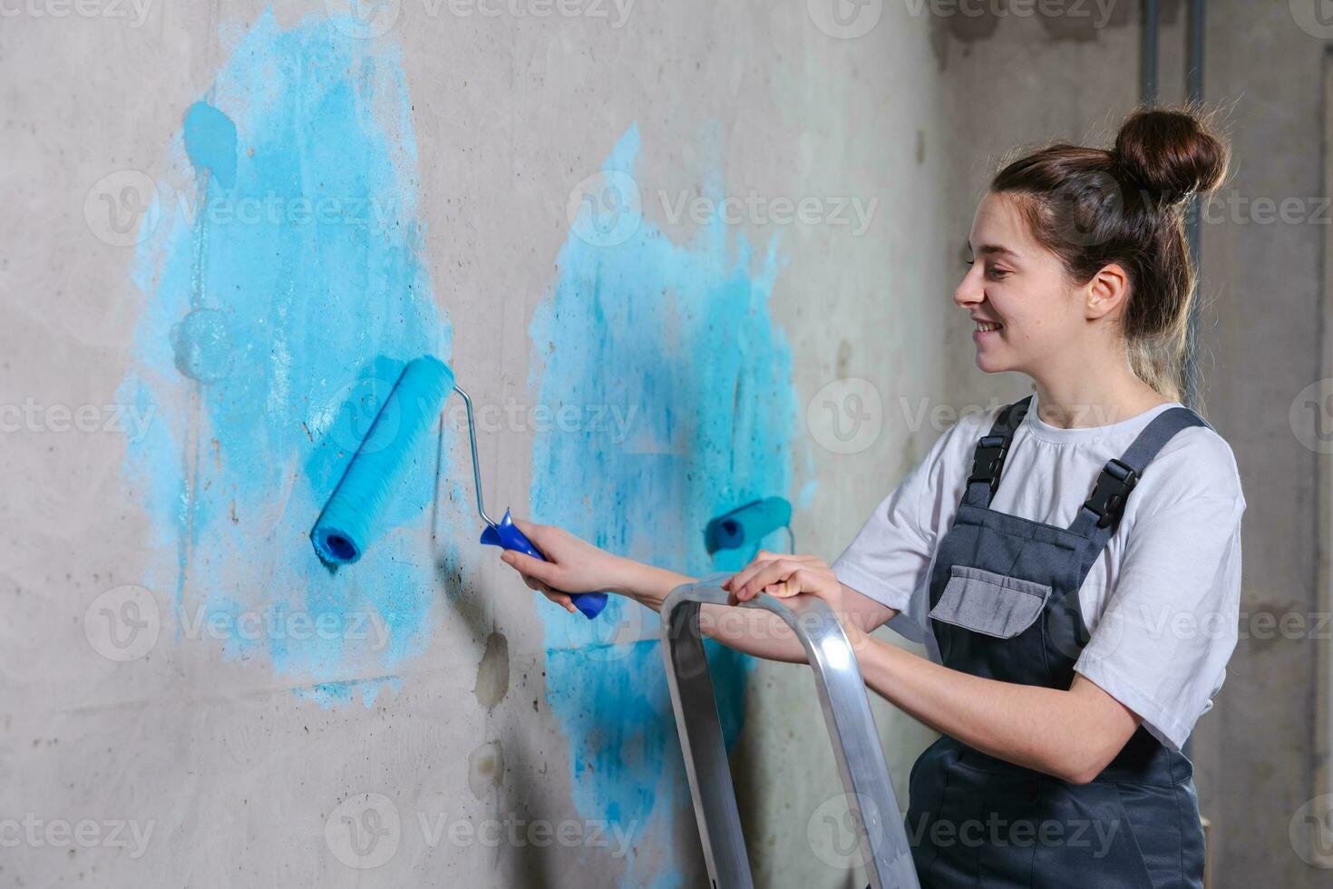 House decoration DIY renovation concept. Happy couple in empty room of new home painting wall together. Husband and wife holding paint roller painting wall with blue color paint in new house. photo