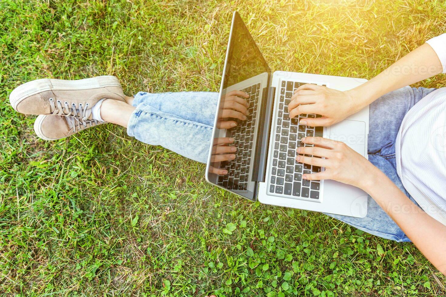 Woman legs on green grass lawn in city park, hands working on laptop pc computer. Freelance business concept photo