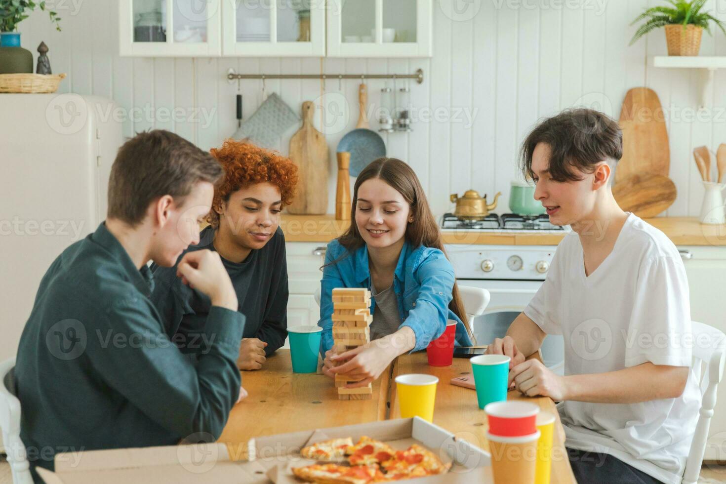 Home party. Friends spending time together playing in board game crash wooden tower at home. Happy diverse group having fun together indoor. Mixed race young buddies best friends enjoying weekend. photo