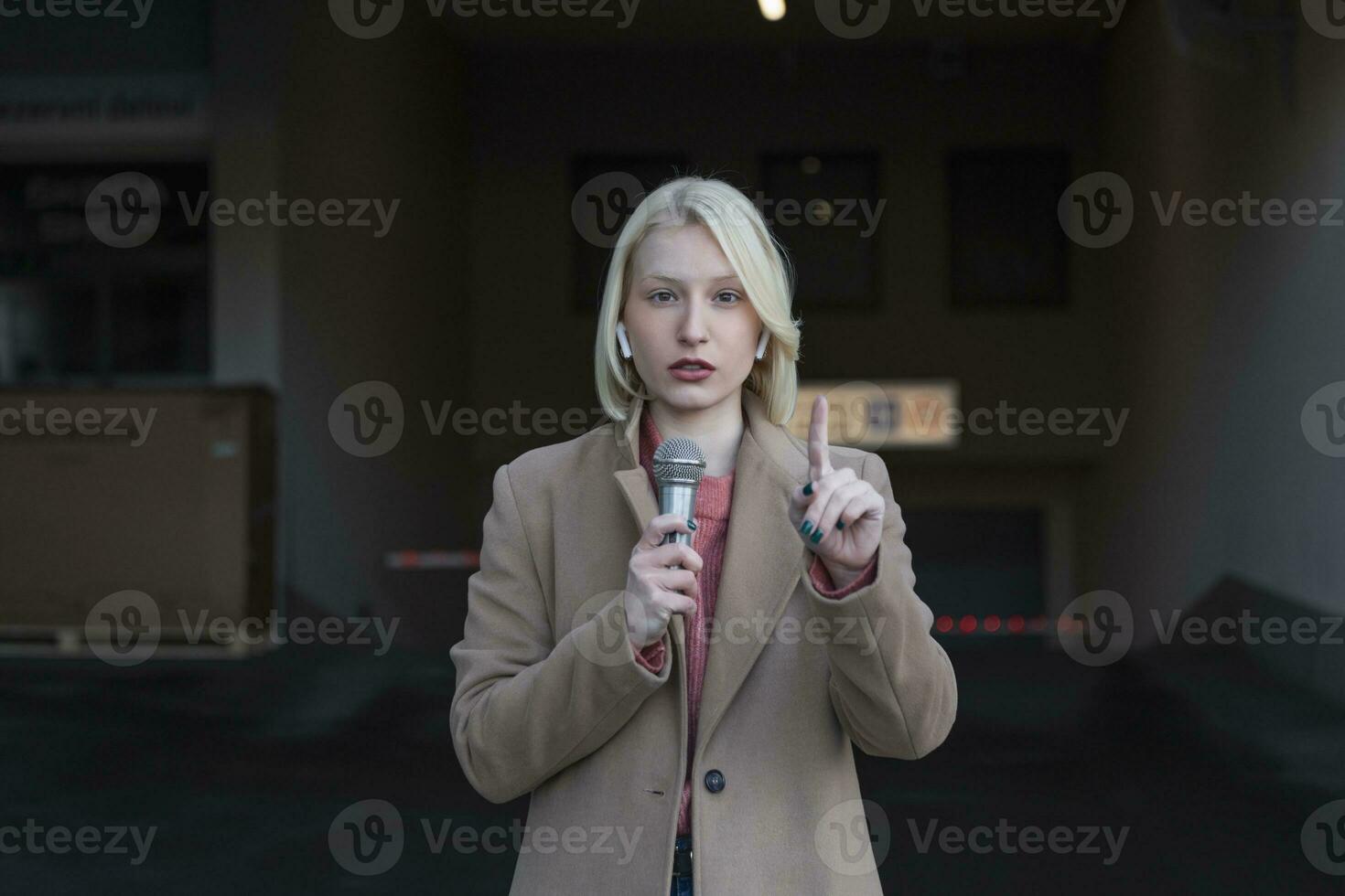 Cropped portrait of professional female reporter at work. Young woman standing on the street with a microphone in hand and smiling at camera. Horizontal shot. Selective focus on woman photo