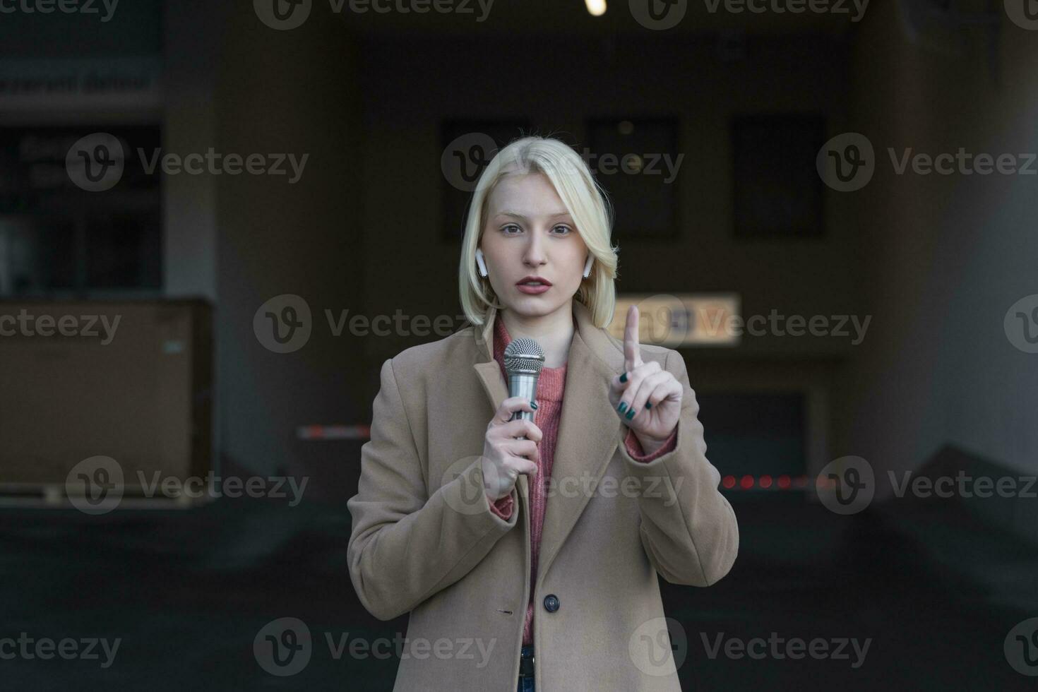 recortado retrato de profesional hembra reportero a trabajar. joven mujer en pie en el calle con un micrófono en mano y sonriente a cámara. horizontal disparo. selectivo atención en mujer foto