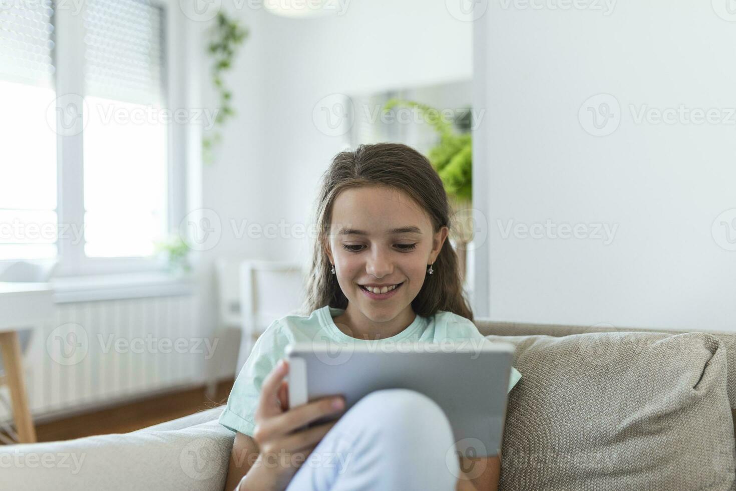 cute little happy girl smile sitting down on sofa using looking digital tablet pad in the living room at home. family activity concept. photo