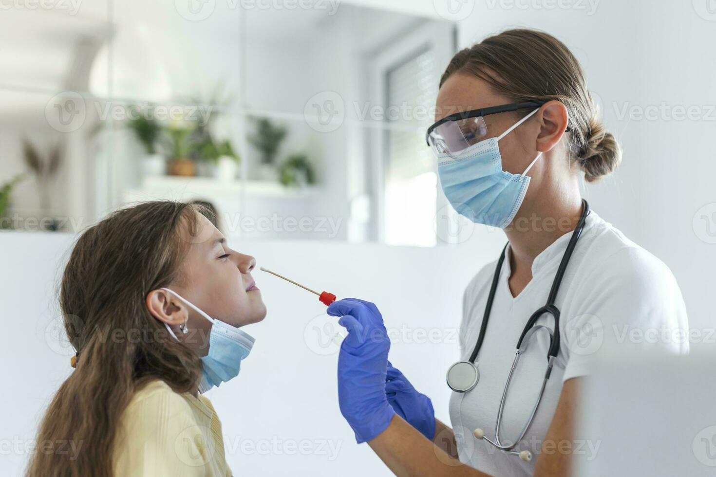 Nurse performing a nose swab test on a little child. Girl going through PCR testing due to COVID-19 pandemic. Female doctor using cotton swab while PCR testing small girl photo