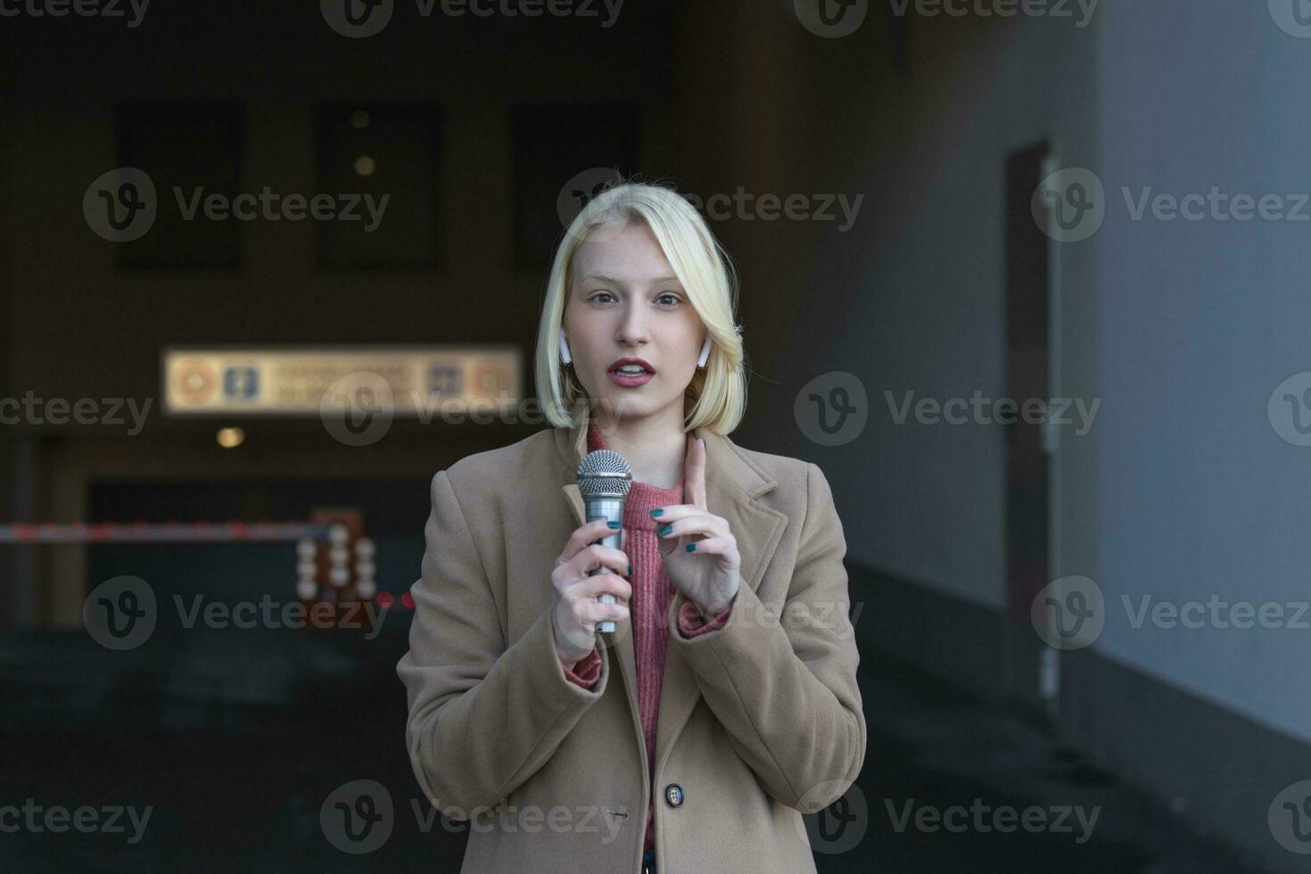 Cropped portrait of professional female reporter at work. Young woman standing on the street with a microphone in hand and smiling at camera. Horizontal shot. Selective focus on woman photo