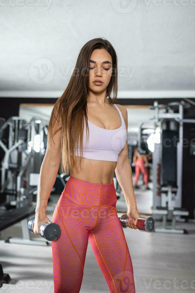 deportivo mujer lo hace el ejercicios con pesas en el gimnasia. foto de muscular mujer en ropa de deporte en deporte club. fuerza y motivación.