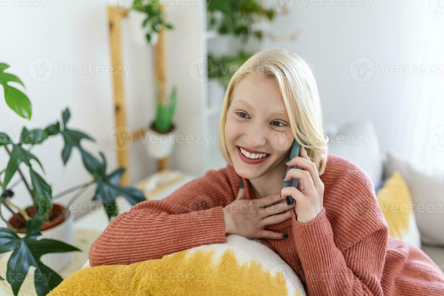 Attractive smiling woman using smart phone while sitting on the sofa at home. Communication and coziness concept. photo