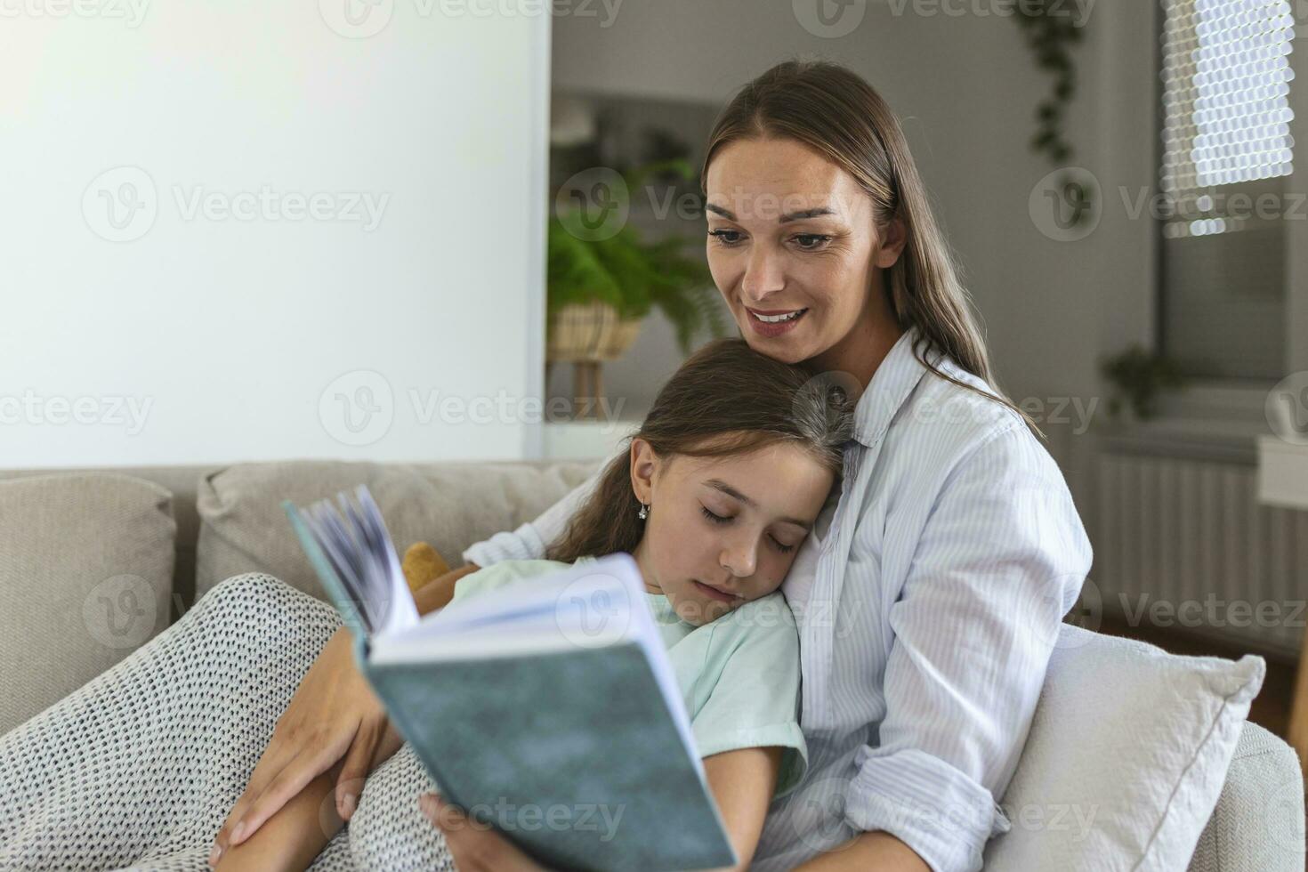 Loving young mother reading book to adorable little daughter, sitting on cozy sofa in living room, mum teaching preschool girl child, family spending weekend at home together, children education photo