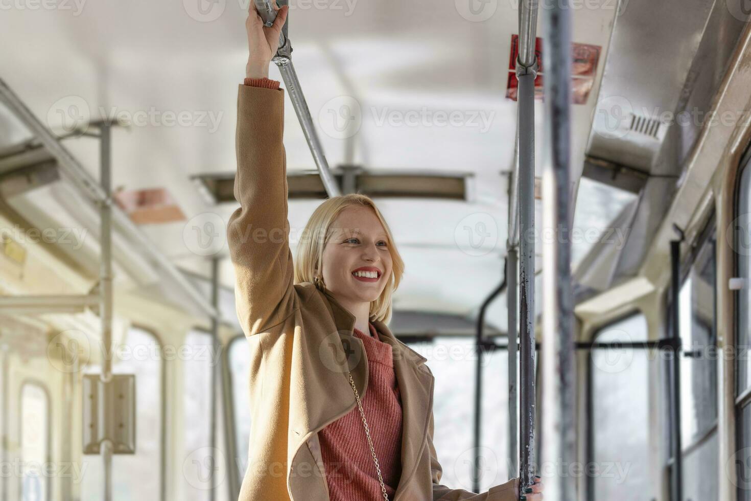 Young woman holding handle while moving in the old tram. Happy passenger enjoying trip at the public transport photo