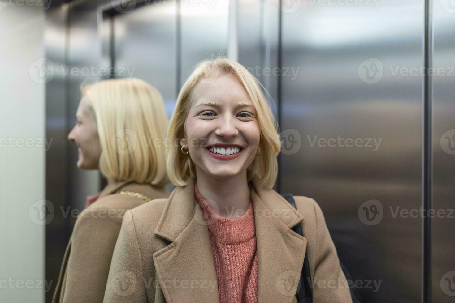 Cute blond female in trendy coat staying in lift alone and smiling, Woman in elevator photo