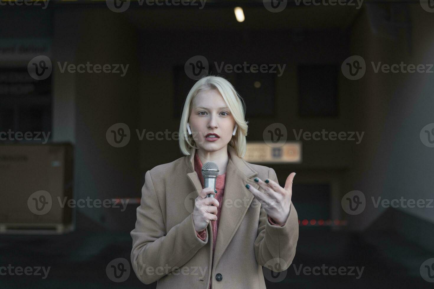 Cropped portrait of professional female reporter at work. Young woman standing on the street with a microphone in hand and smiling at camera. Horizontal shot. Selective focus on woman photo