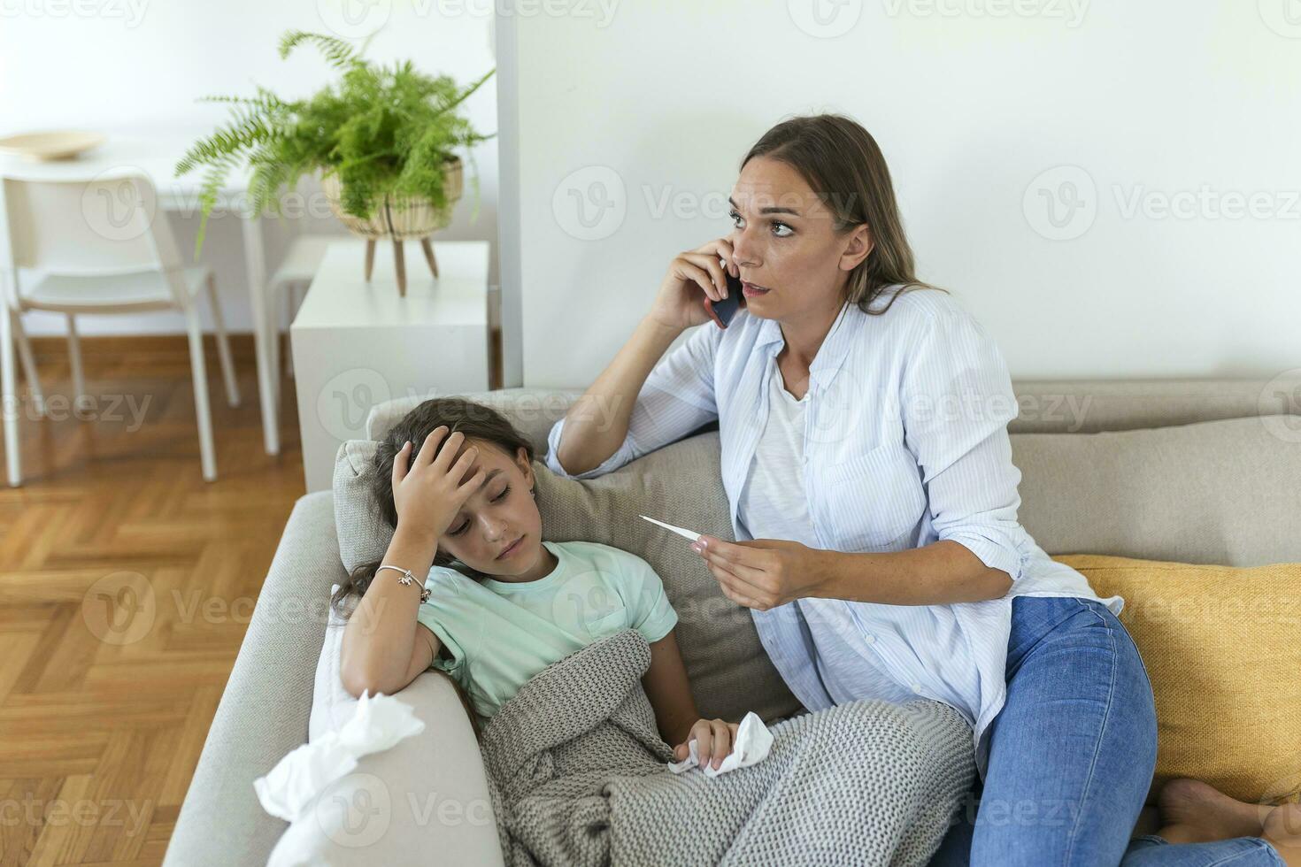 Mother measuring temperature of her ill kid. Sick child with high fever laying in bed and mother holding thermometer. Mother with cell phone calling to doctor photo