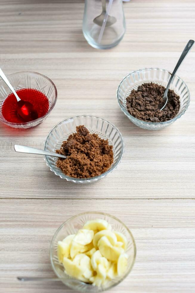 Ingredients of sundae dish as a part of non fire cooking which includes vanilla ice cream, brownie, coco powder, freshly chopped fruits and strawberry syrup. Preparation of sundae dish photo