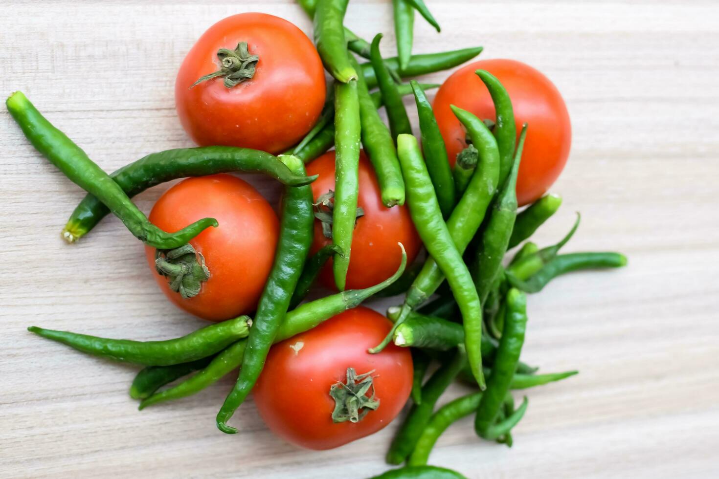 Red tomato and green chili pepper on plain wooden table, green essential vegetables for all essential foods, view of unpeeled vegetables with plain background photo