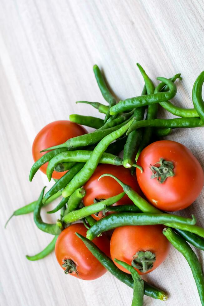 Red tomato and green chili pepper on plain wooden table, green essential vegetables for all essential foods, view of unpeeled vegetables with plain background photo