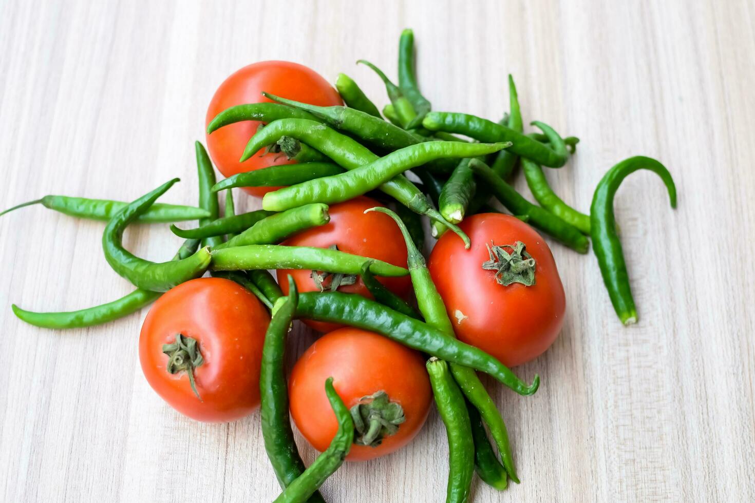 Red tomato and green chili pepper on plain wooden table, green essential vegetables for all essential foods, view of unpeeled vegetables with plain background photo