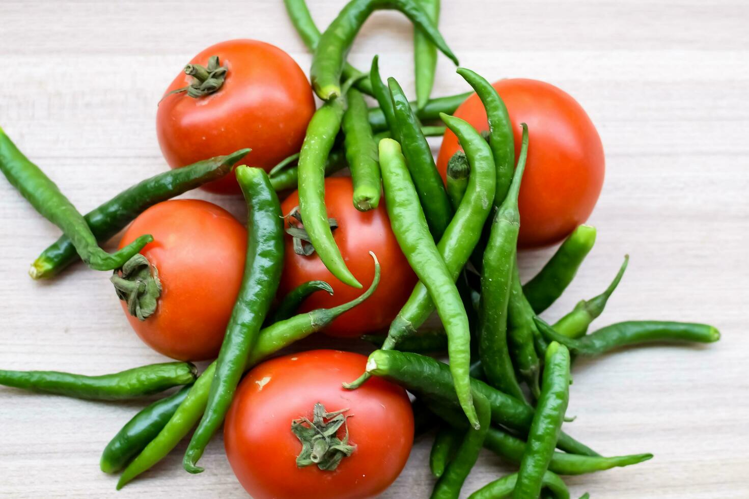Red tomato and green chili pepper on plain wooden table, green essential vegetables for all essential foods, view of unpeeled vegetables with plain background photo