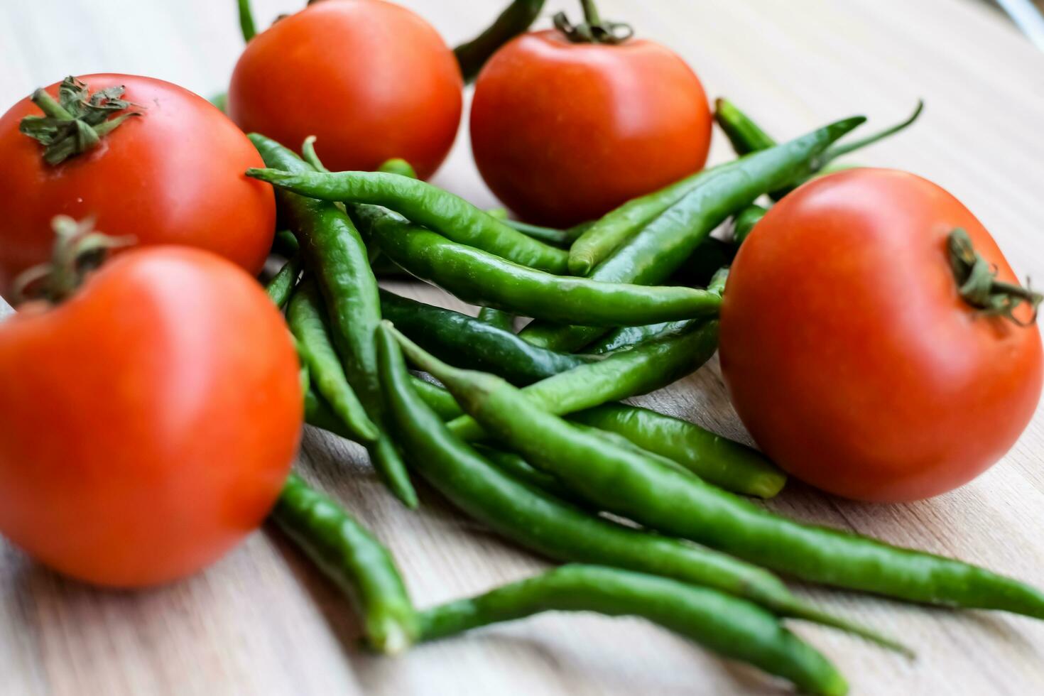 Red tomato and green chili pepper on plain wooden table, green essential vegetables for all essential foods, view of unpeeled vegetables with plain background photo