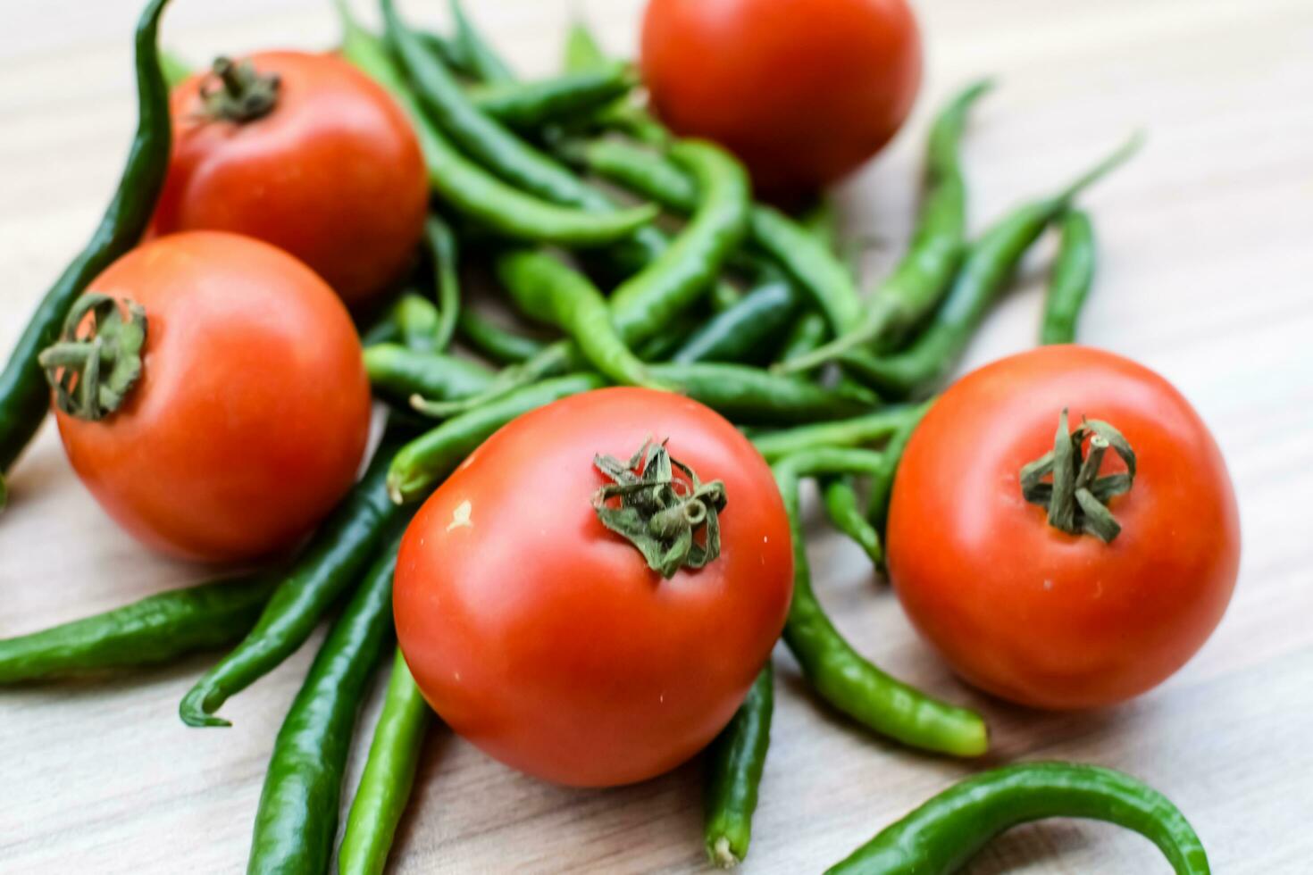 Red tomato and green chili pepper on plain wooden table, green essential vegetables for all essential foods, view of unpeeled vegetables with plain background photo