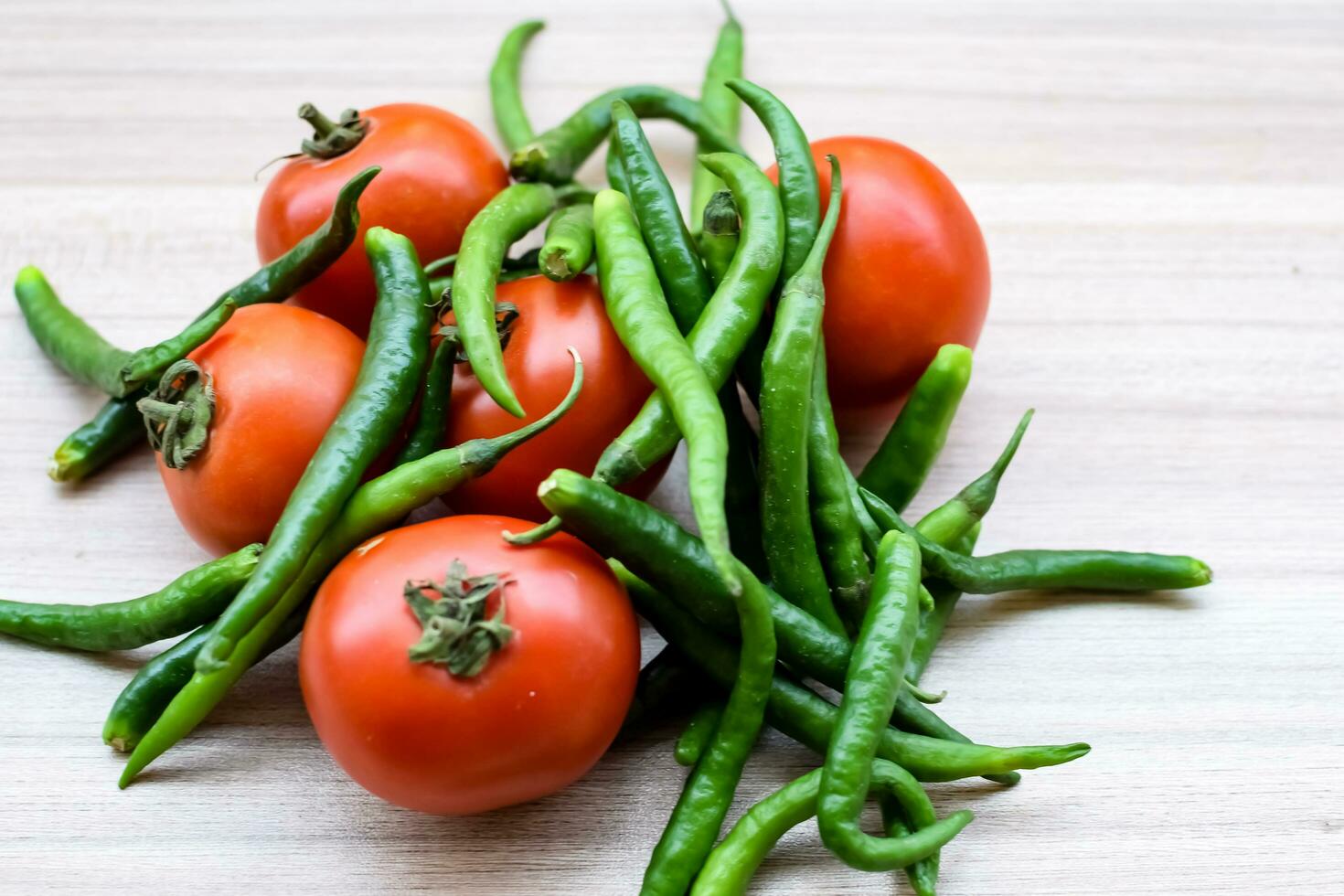Red tomato and green chili pepper on plain wooden table, green essential vegetables for all essential foods, view of unpeeled vegetables with plain background photo