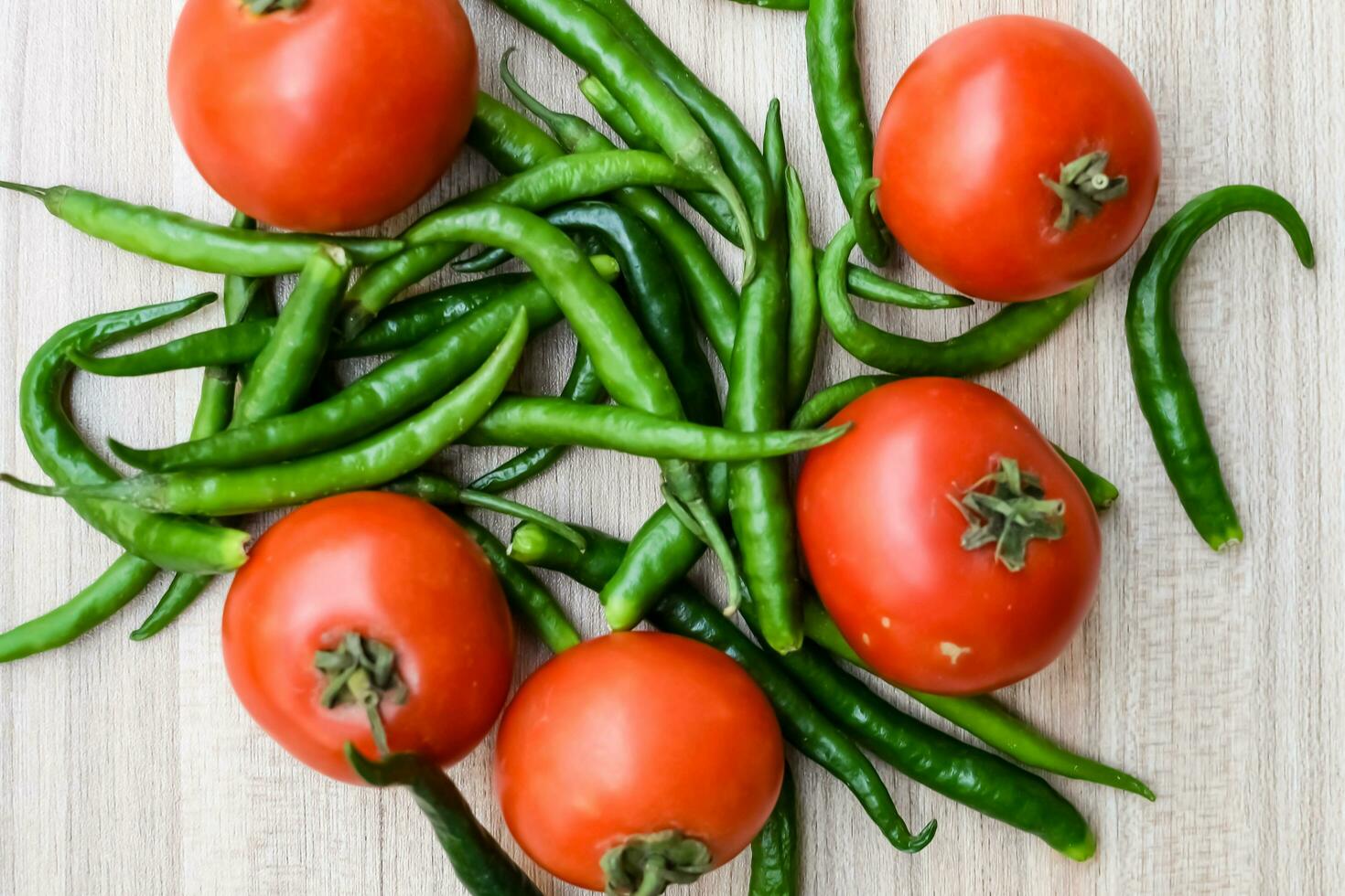 Red tomato and green chili pepper on plain wooden table, green essential vegetables for all essential foods, view of unpeeled vegetables with plain background photo