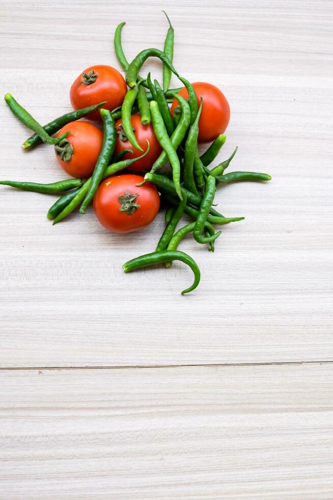 Red tomato and green chili pepper on plain wooden table, green essential vegetables for all essential foods, view of unpeeled vegetables with plain background photo