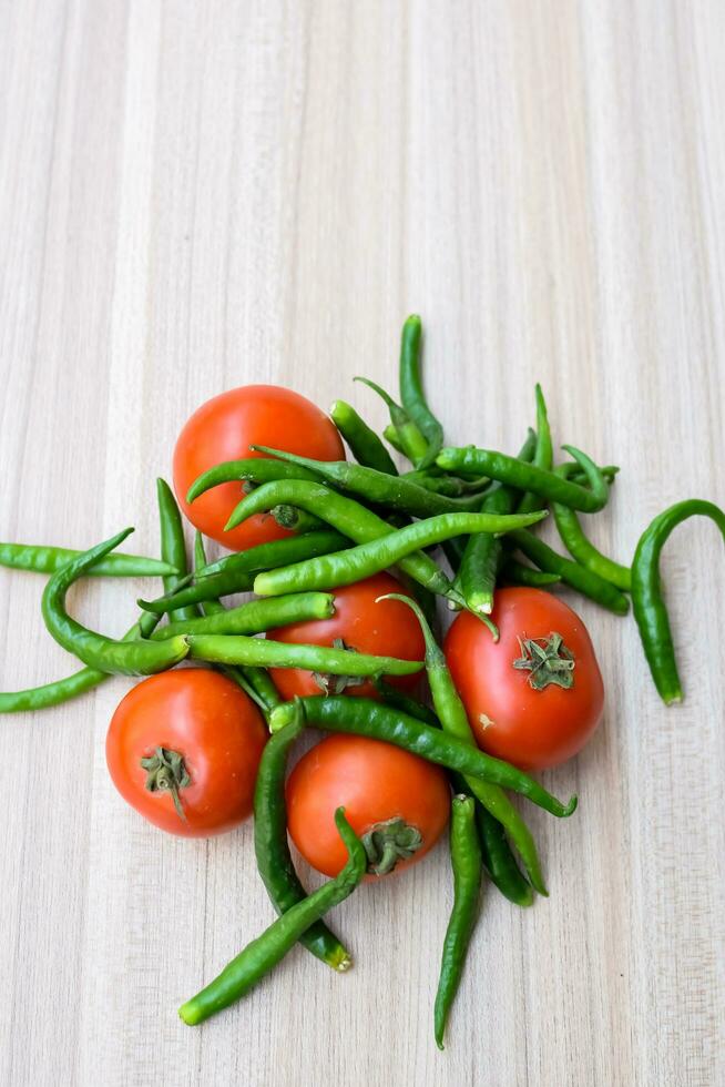 Red tomato and green chili pepper on plain wooden table, green essential vegetables for all essential foods, view of unpeeled vegetables with plain background photo