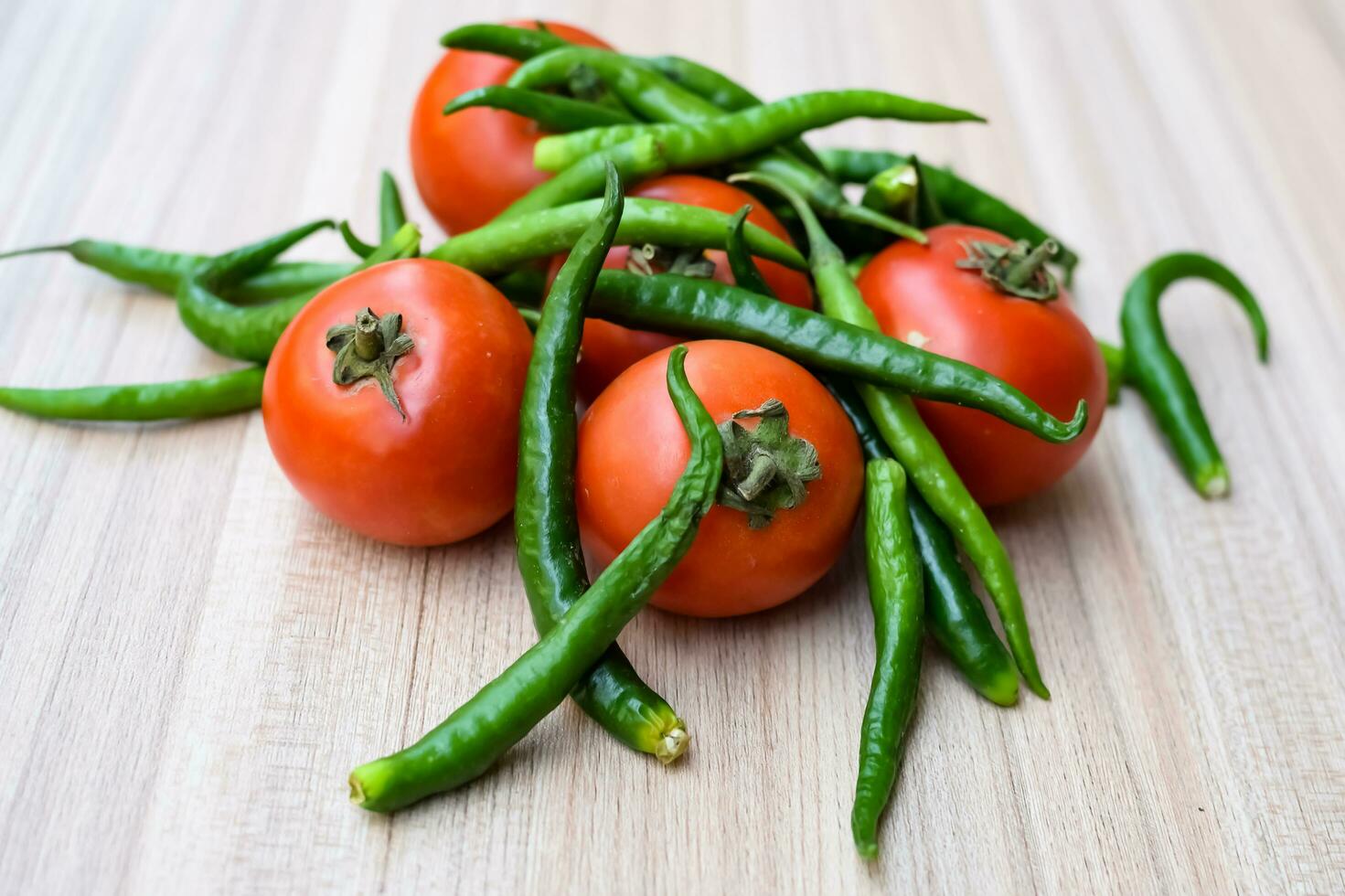 Red tomato and green chili pepper on plain wooden table, green essential vegetables for all essential foods, view of unpeeled vegetables with plain background photo