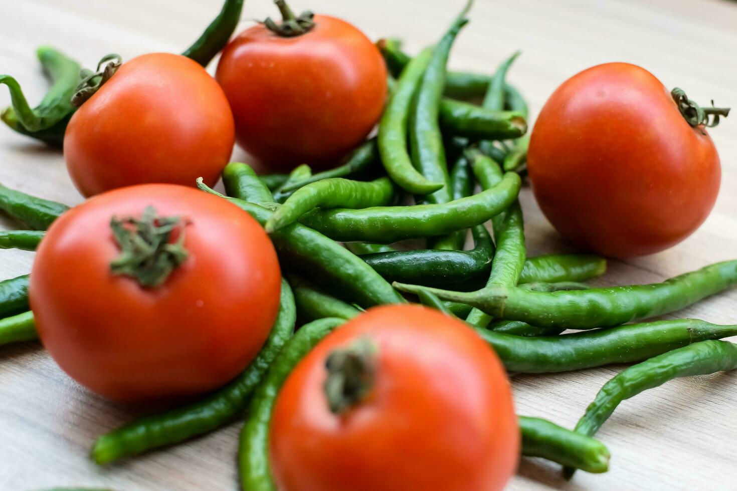 Red tomato and green chili pepper on plain wooden table, green essential vegetables for all essential foods, view of unpeeled vegetables with plain background photo