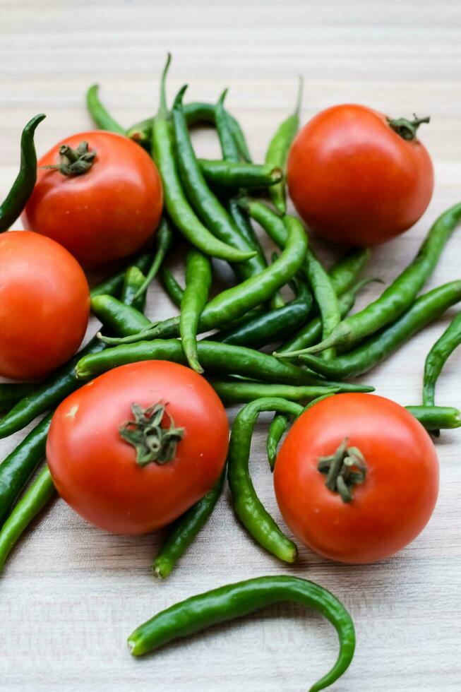 Red tomato and green chili pepper on plain wooden table, green essential vegetables for all essential foods, view of unpeeled vegetables with plain background photo
