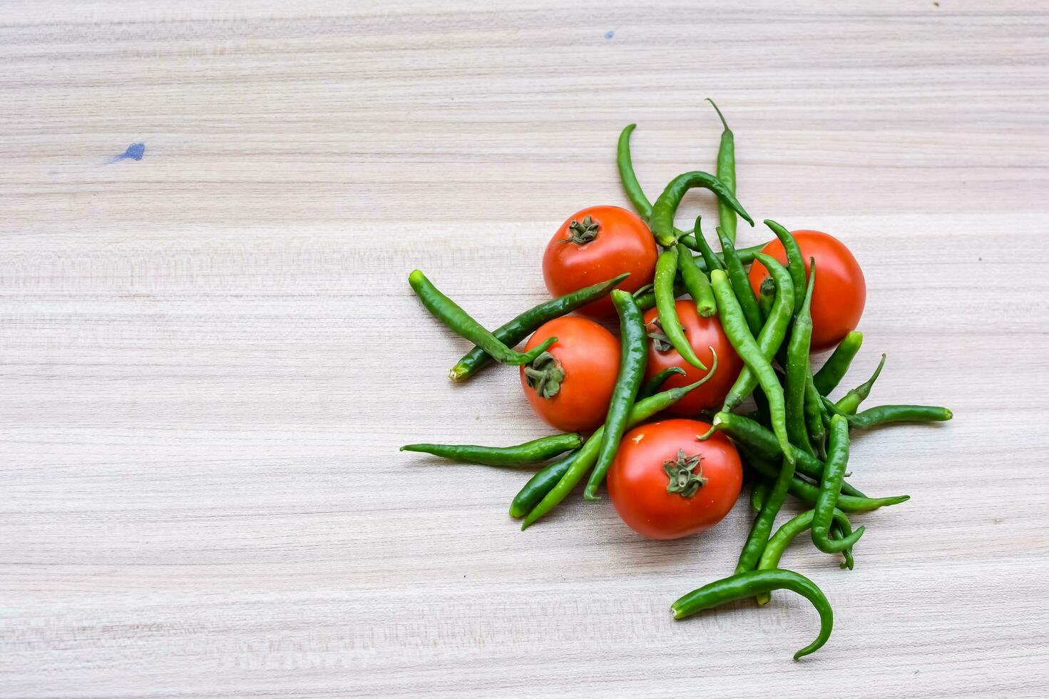 Red tomato and green chili pepper on plain wooden table, green essential vegetables for all essential foods, view of unpeeled vegetables with plain background photo