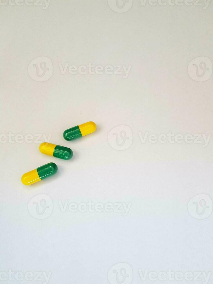 Isolated white photo of three medicine capsules green and yellow.