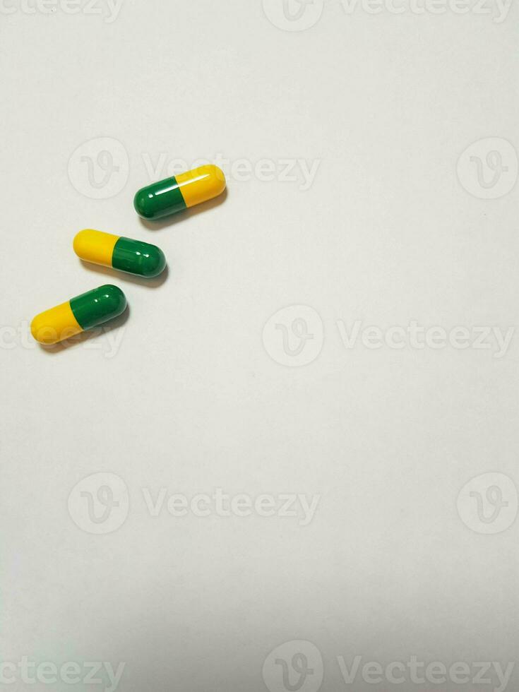 Isolated white photo of three medicine capsules green and yellow.