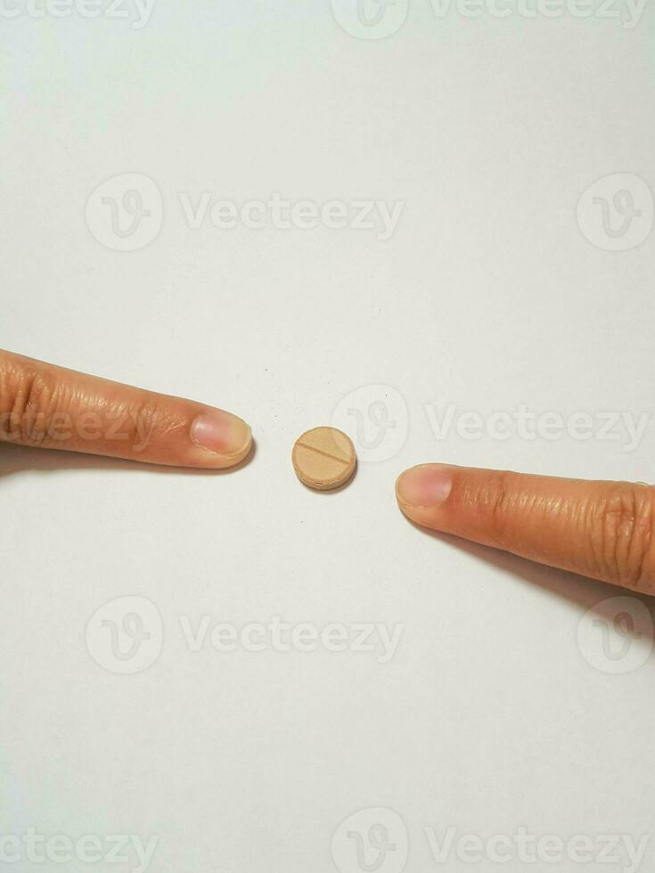 Isolated white photo of two forefingers pointing at a brown medicine tablet.