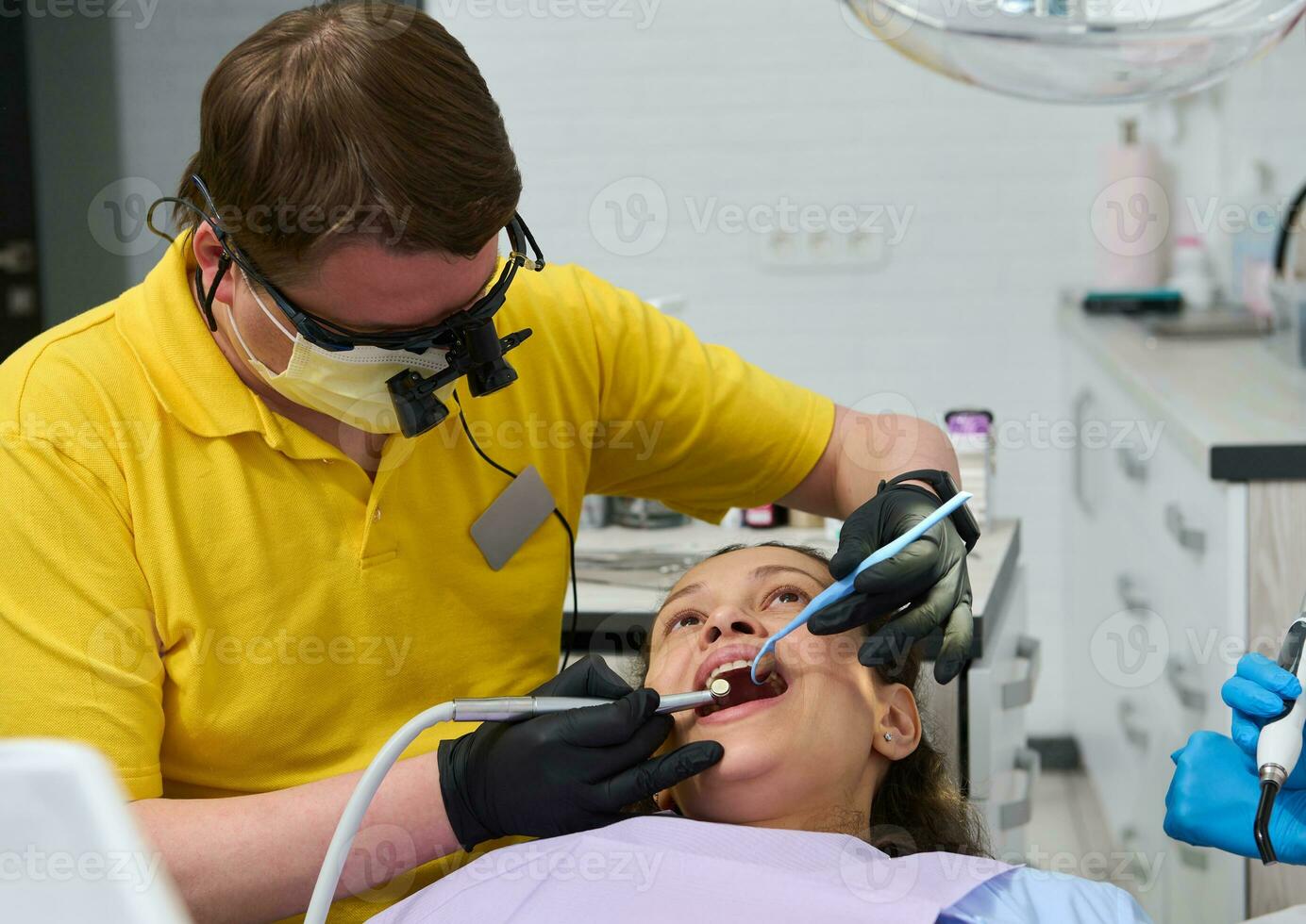 profesional dentista vistiendo ortodoncista prismáticos examina dientes y realiza tratamiento a un paciente en dental clínica foto