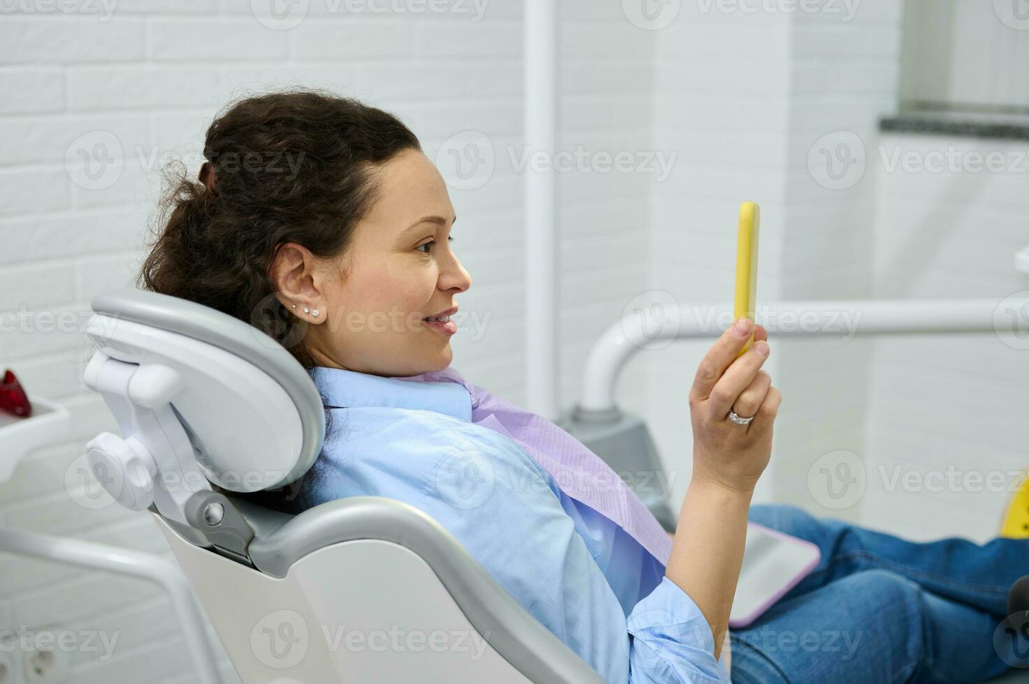 contento hembra paciente en dentista silla, sonrisas mirando en espejo, satisfecho con tratamiento, profesional dientes blanqueo foto