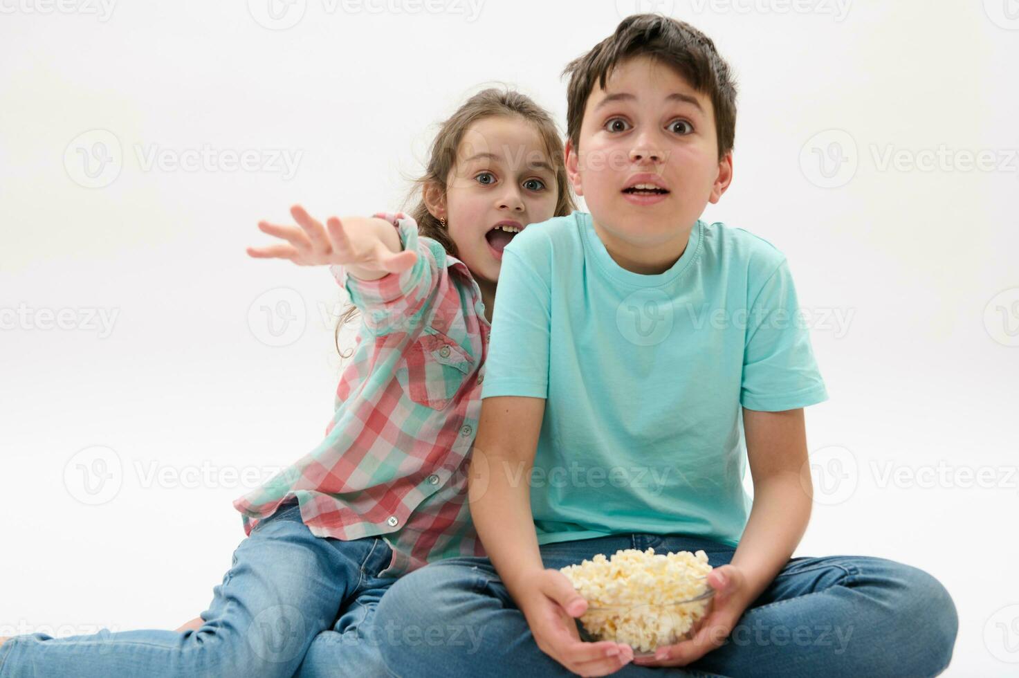 Adorable children with bowl of popcorn, watching scary or fantasy movie, expressing fright and fear on white background photo