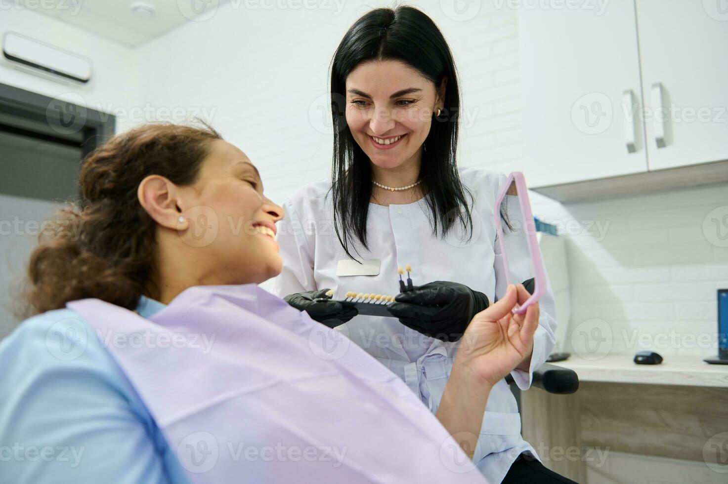 Smiling happy woman looking at her mirror reflection after teeth whitening procedure in dentistry clinic photo