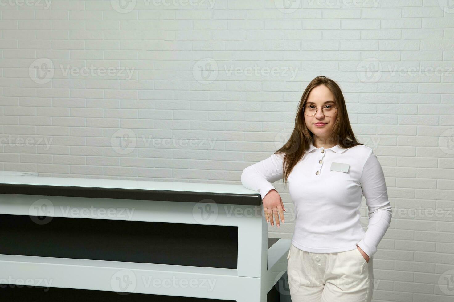 Portrait of a pleasant young woman receptionist, administrator at reception desk of a medical clinic, looking at camera photo