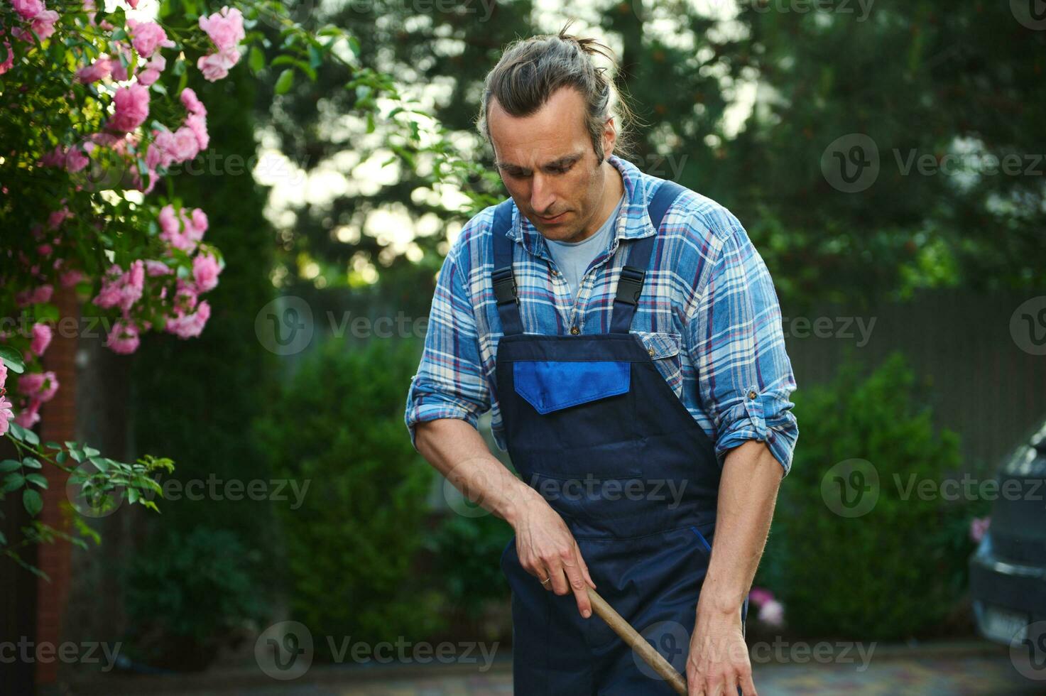 cintura arriba retrato de un hermoso caucásico hombre jardinero en trabajo uniforme, limpieza el malas hierbas desde el losas en patio interior foto