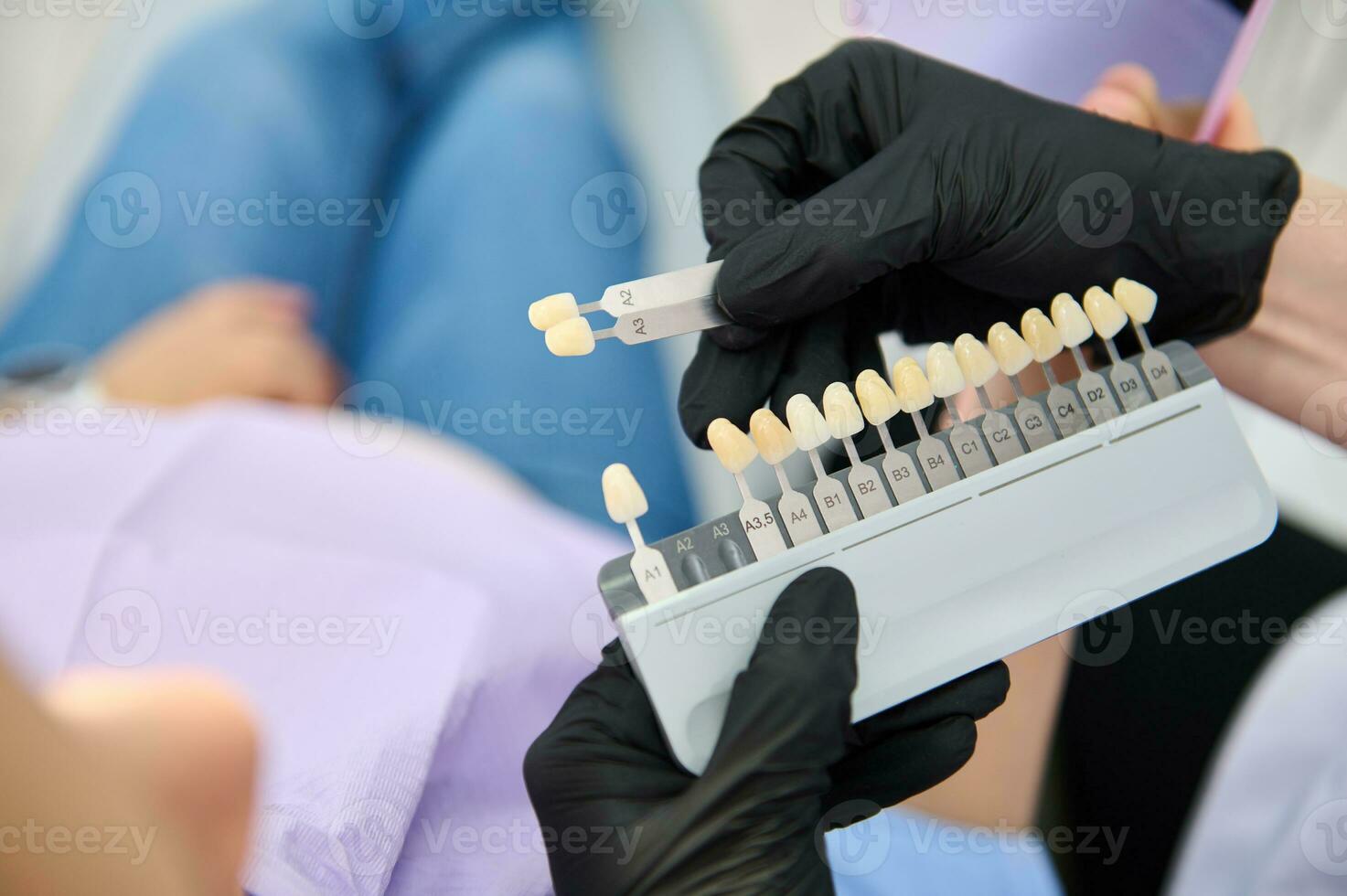 Close-up dentist's hands hold tooth color chart, Vita scale, teeth bleaching guide over patient sitting in dental chair photo