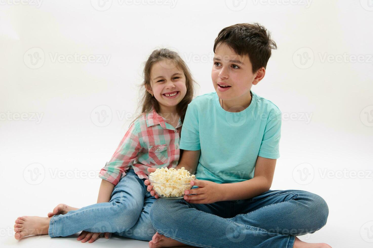 Mischievous adorable children, a teen boy and preschooler girl have fun together, eat popcorn and watch movie or cartoon photo