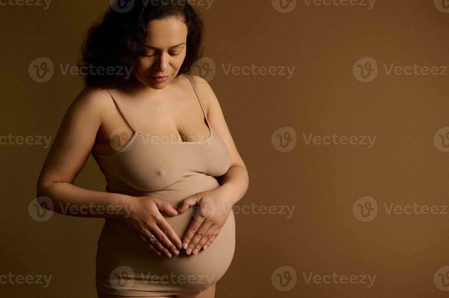 hermosa embarazada mujer manos formando corazón en su barriguita con su manos, aislado en beige antecedentes. Copiar anuncio espacio foto