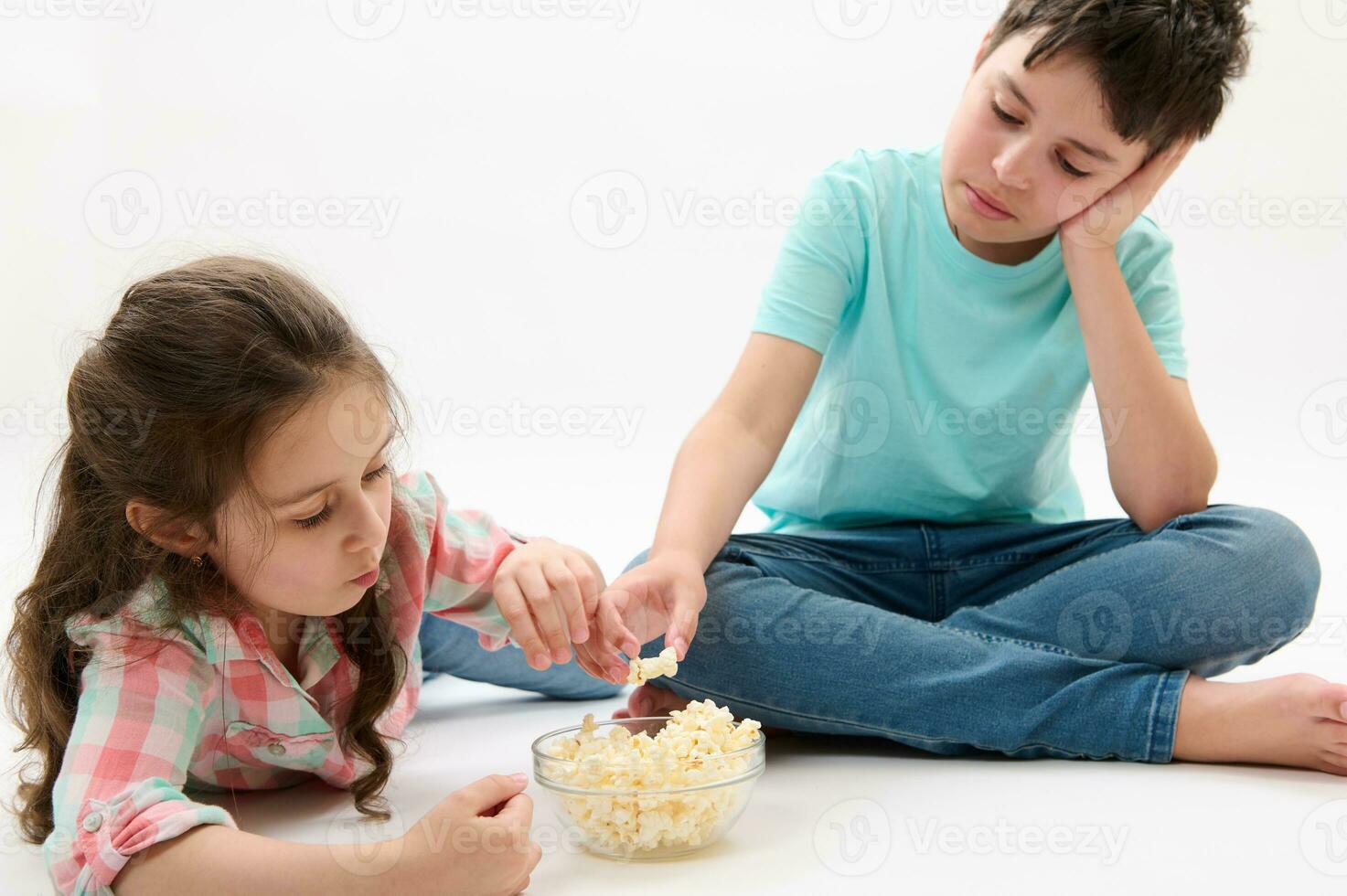 contento primario colegio niños - adolescente hermano y su mas joven hermana comiendo Palomitas, aislado en blanco estudio antecedentes. foto