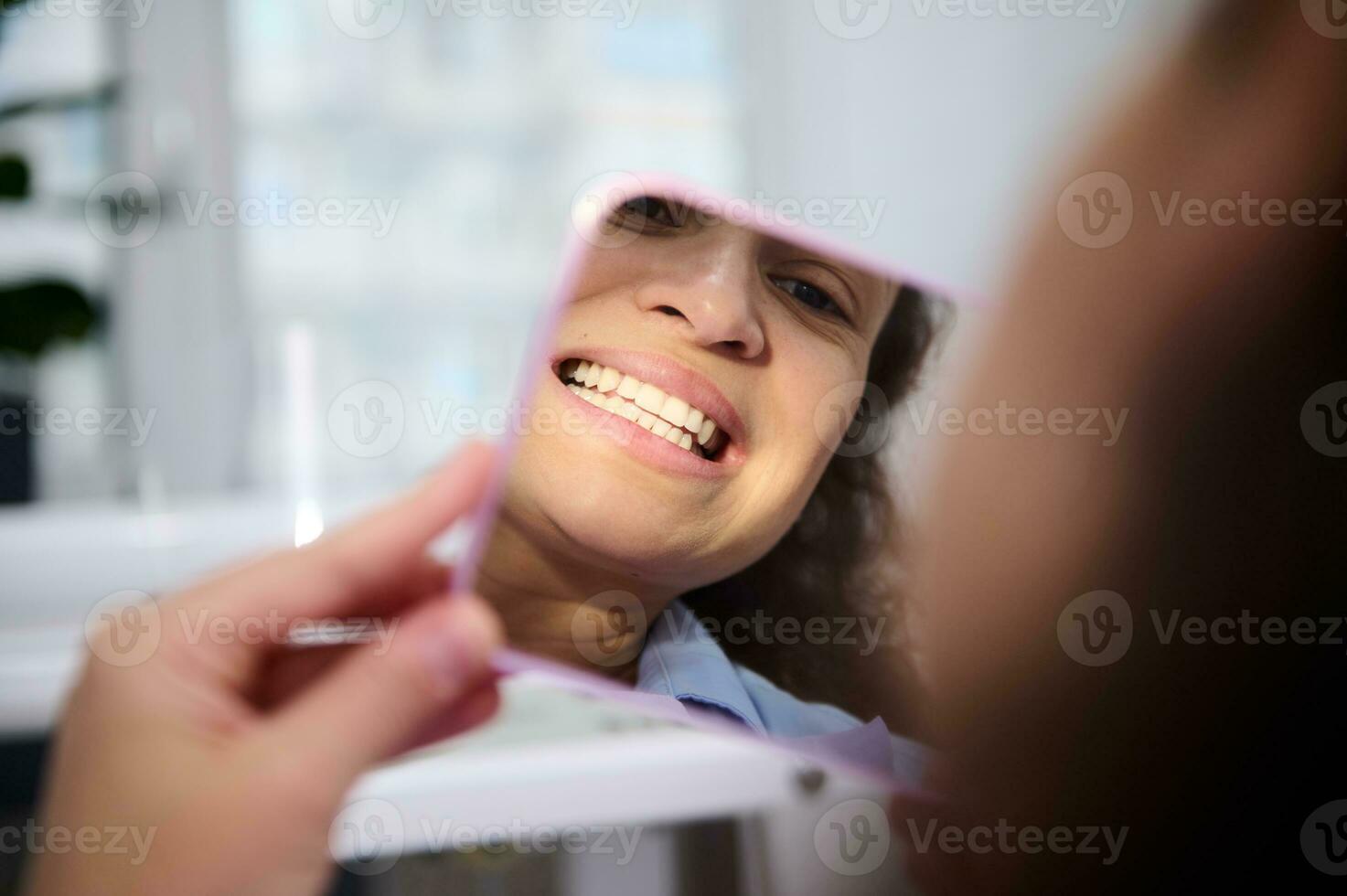 Reflection in mirror of a female patient in dental chair, admiring her smile and teeth after teeth bleaching procedure photo