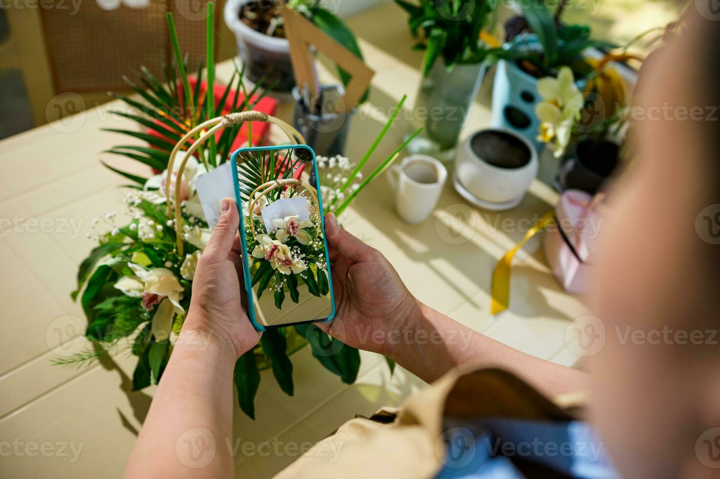 Close-up florist holds smartphone, photographing a bouquet of flowers in wicker basket, created in floral design studio photo