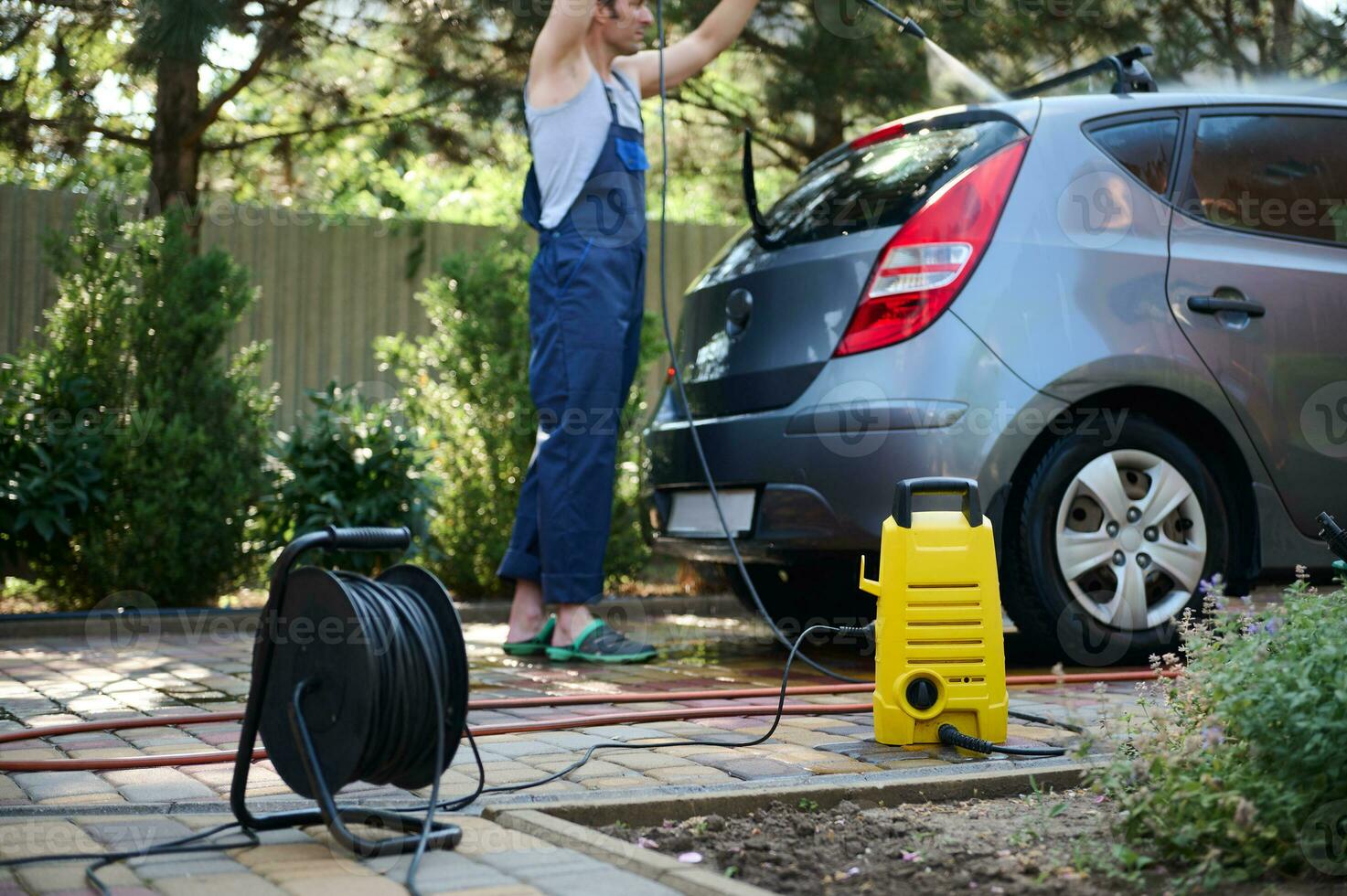 Focus on water high pressure cleaner against blurred man directing spray wand with water jet on his car while washing it photo