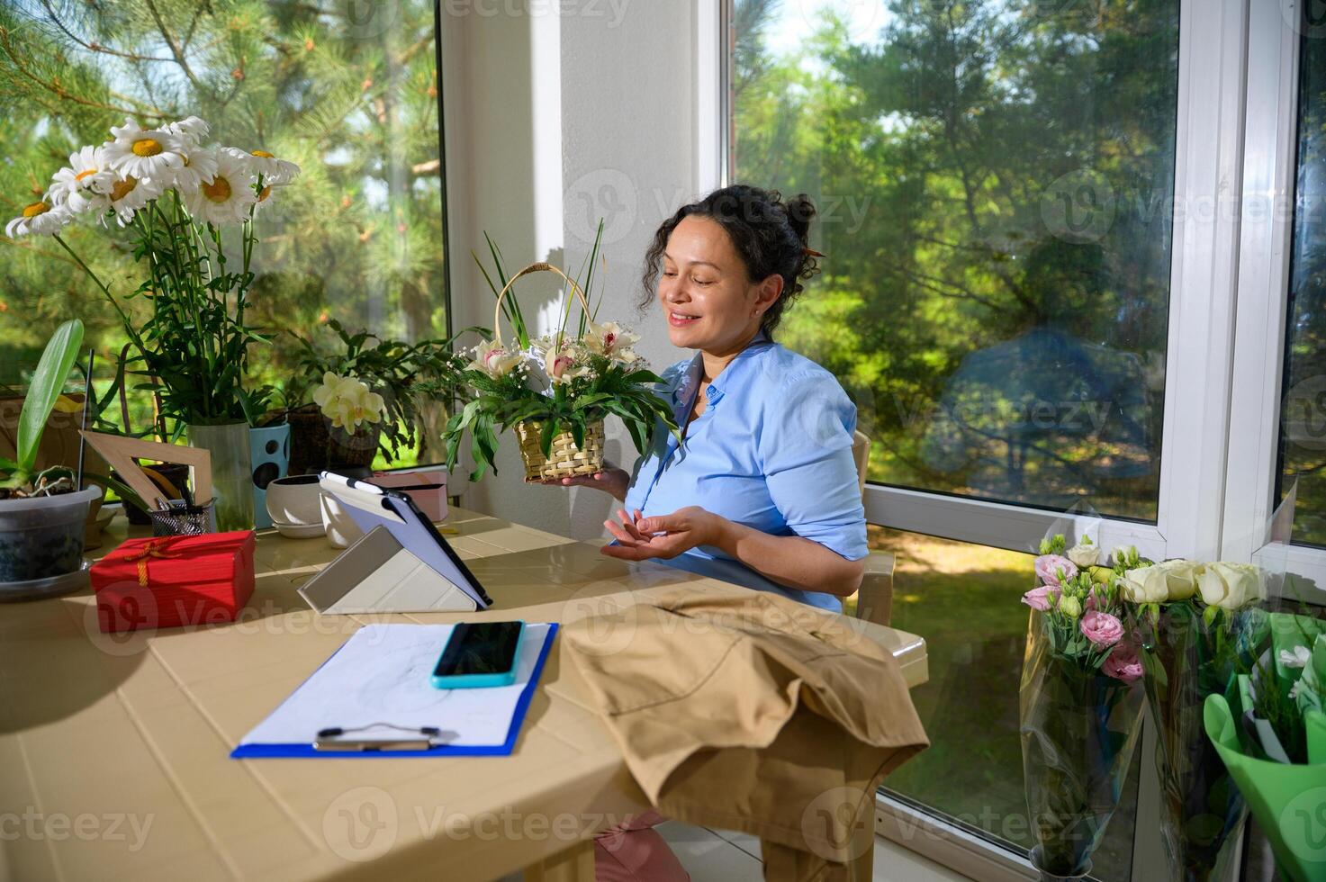 Charming female florist having online video conference with client, sitting at desk with laptop in floral design studio photo