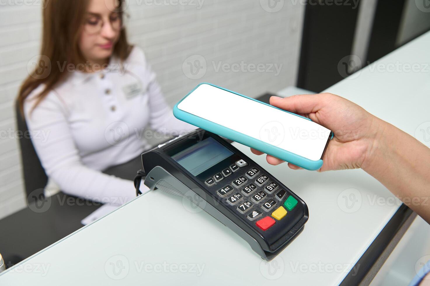 Close-up customer hand holds smartphone with white blank digital scree over credit card reader. Cashless payment via NFC photo